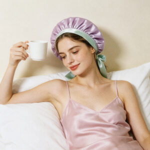 woman enjoying morning coffee in bed wearing lavender reversible silk bonnet with mint bow